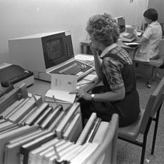 Black and white image of a woman looking at the screen of an early desktop computer