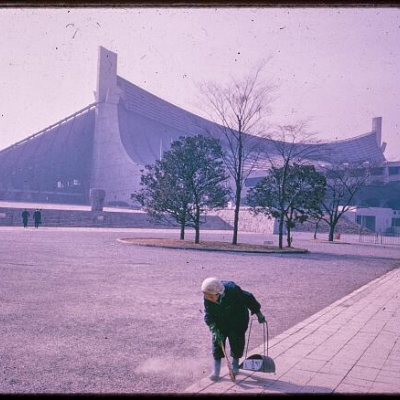 Photograph from "Urbanism" series collected by Paul Rudolph depicting woman cleaning pathway in front of Yoyogi National Gymnasium